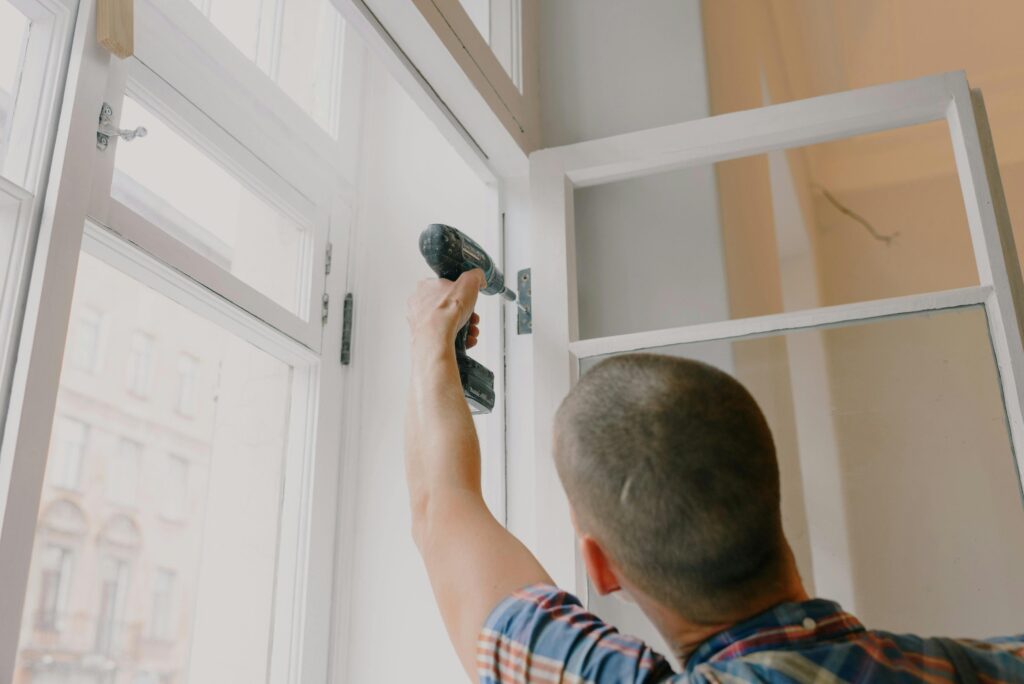 pexels-photo-5691503-5691503 A handyman works with a drill installing window hinges indoors.