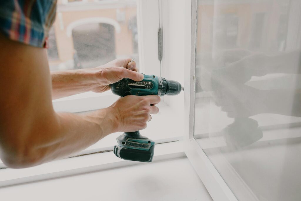 pexels-photo-5768107-5768107 A person using an electric drill to repair or install a window indoors.